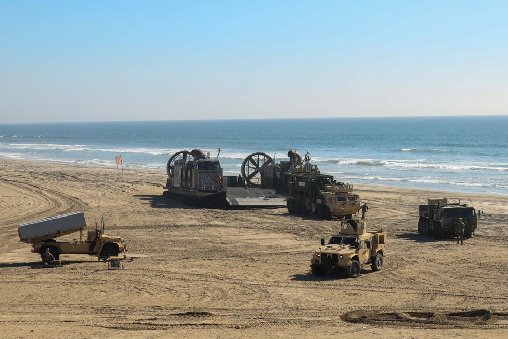 Several military vehicles staged on a beach for an All-Service logistics exercise.